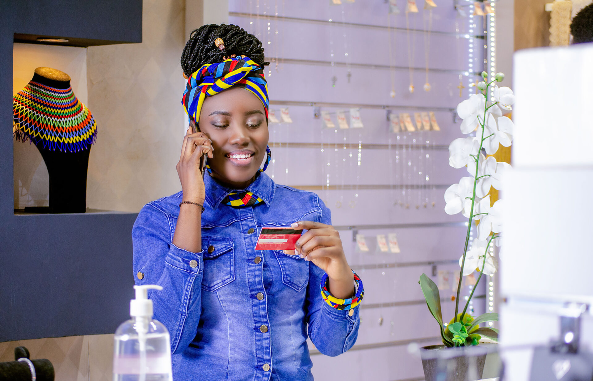 une-jeune-femme-au-travail-qui-tient-un-telephone-et-une-carte-bancaire-en-souriant-dans-un-magasin-de-bijoux