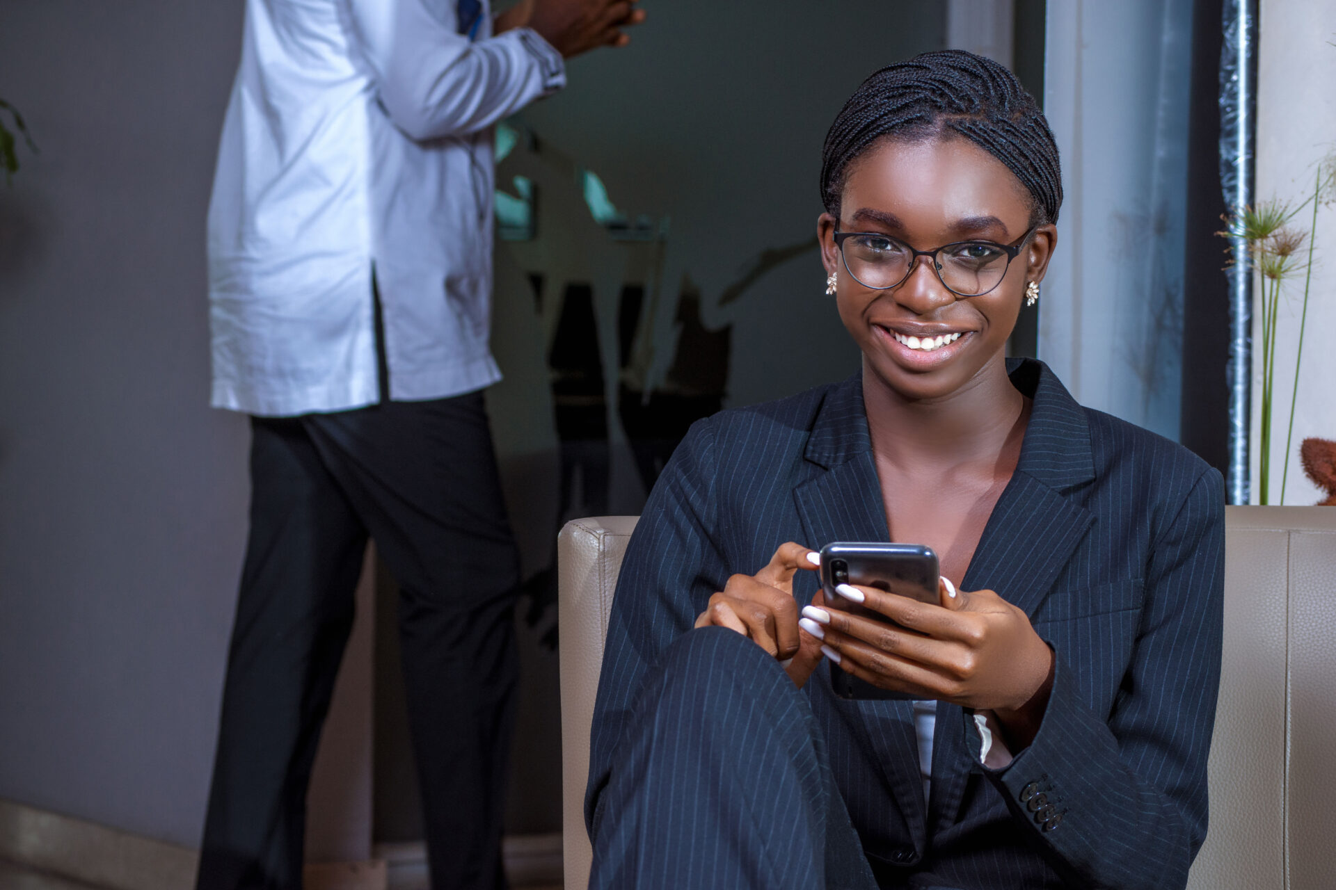 une-femme-noire-africaine-assise-qui-tient-son-telephone-et-sourit-habillee-en-noir