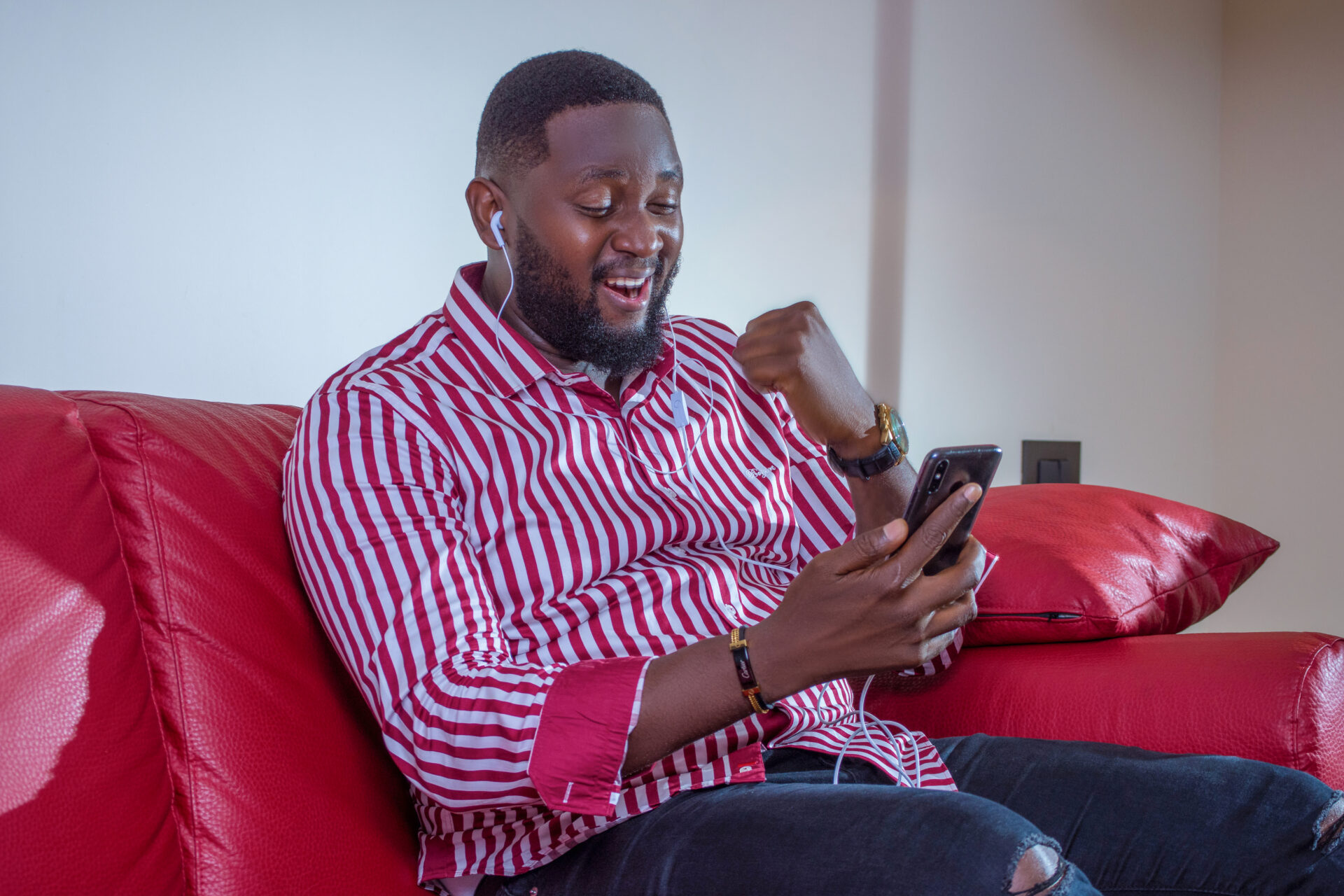 un-jeune-homme-noir-africain-assis-dans-un-fauteuil-qui-regarde-son-telephone-en-se-rejouissant